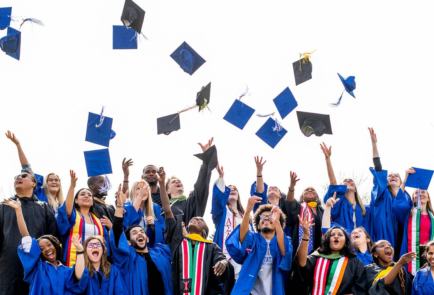Graduates in blue gowns and caps celebrate by tossing their caps into the air.